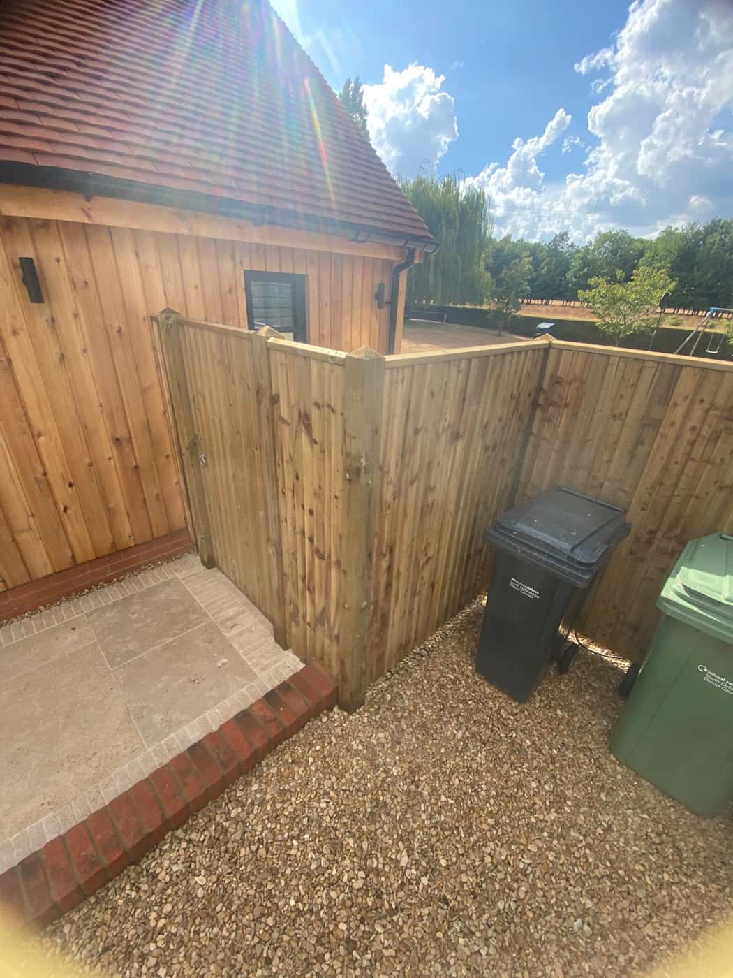 New closeboard fence screening a bin area beside a brick-edged patio