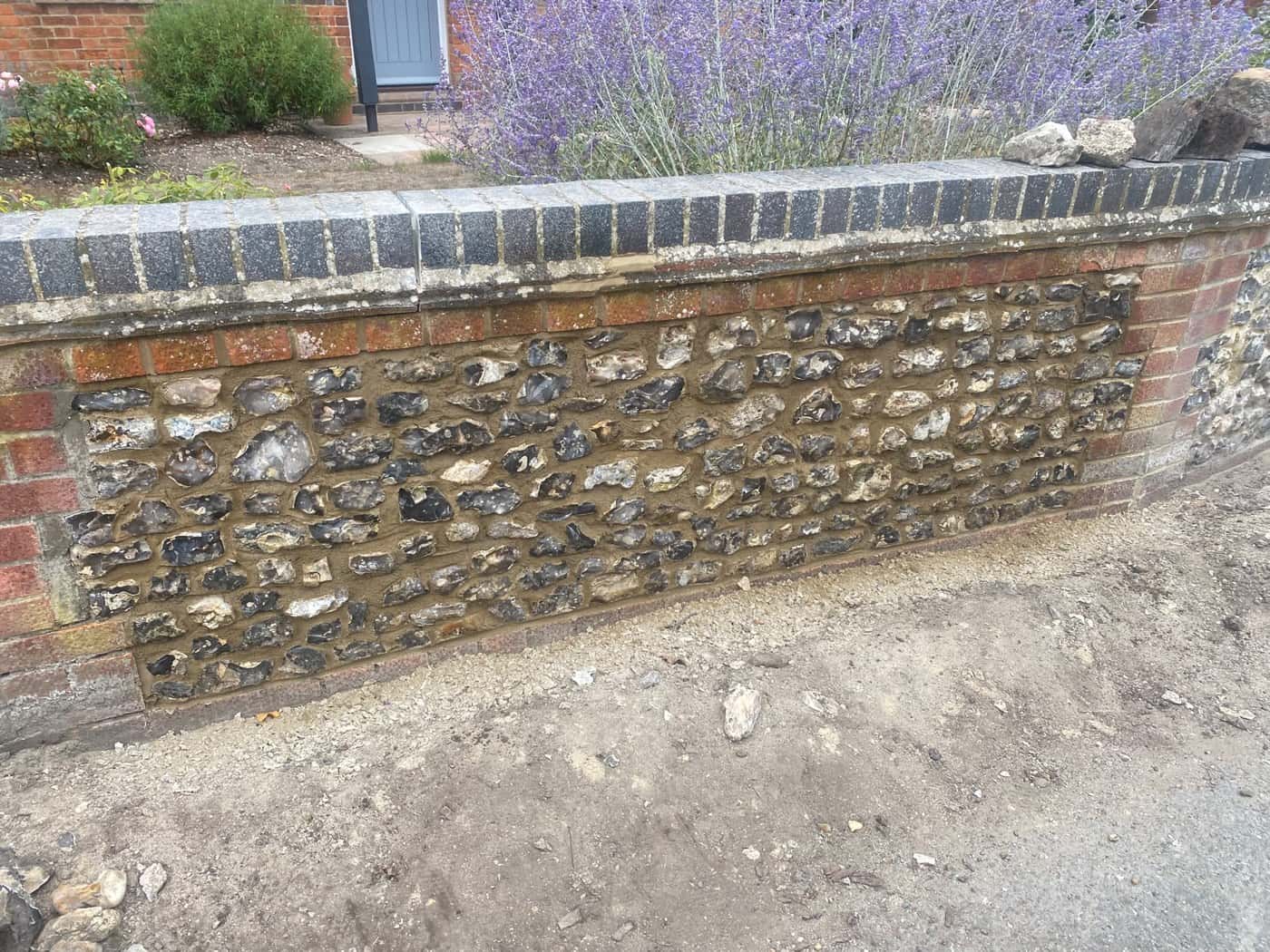 Flint garden wall with red-brick banding and a blue-brick coping