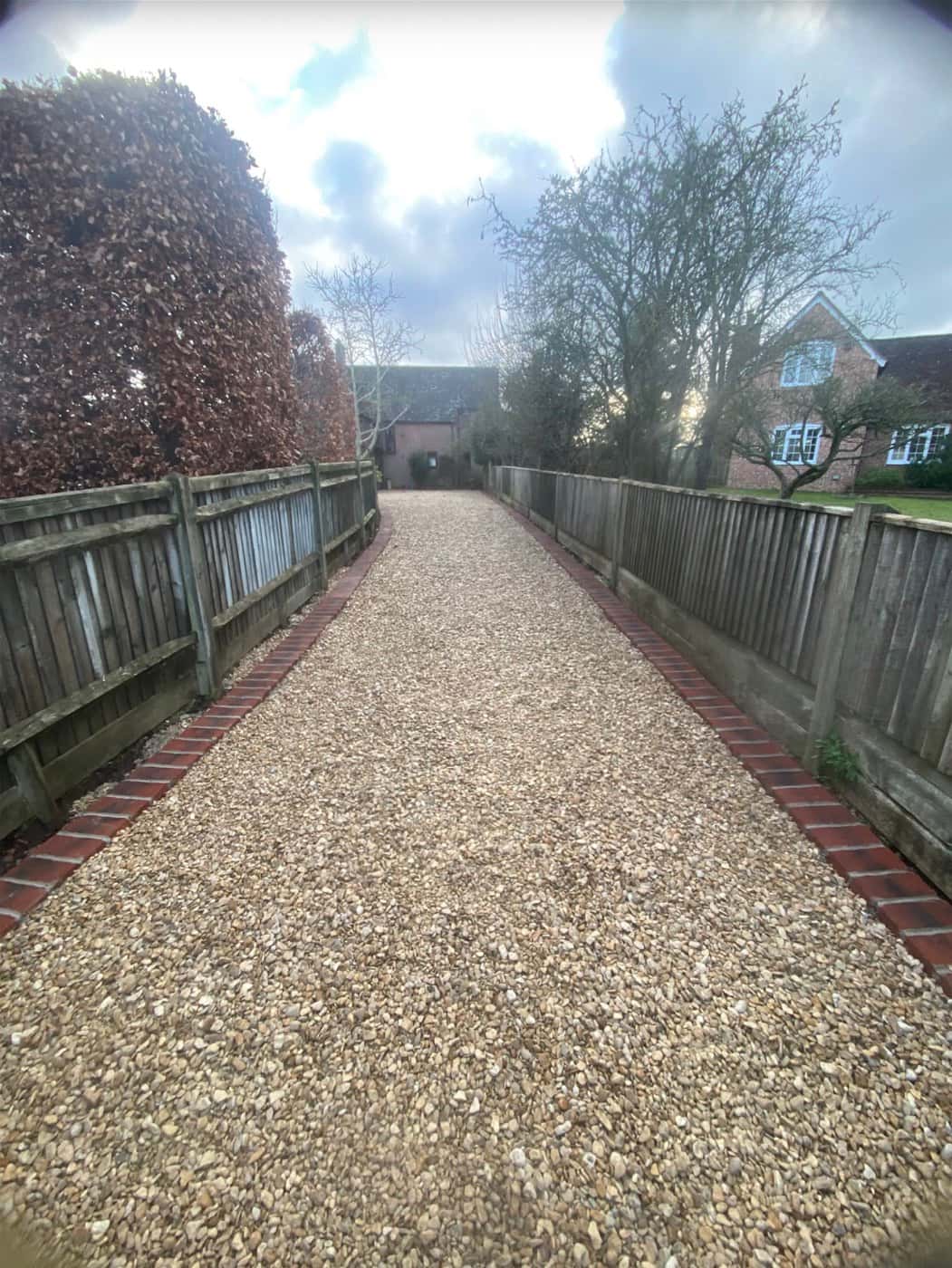 Long gravel driveway with red-brick edging between timber fences