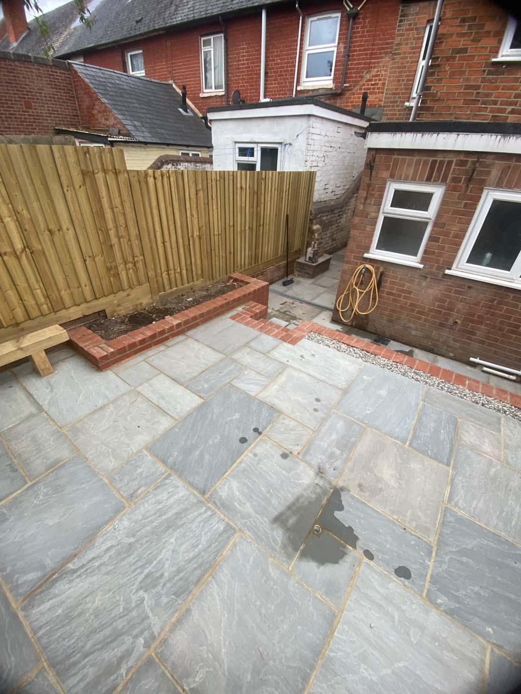 Grey stone patio with a raised brick planter and a new closeboard fence