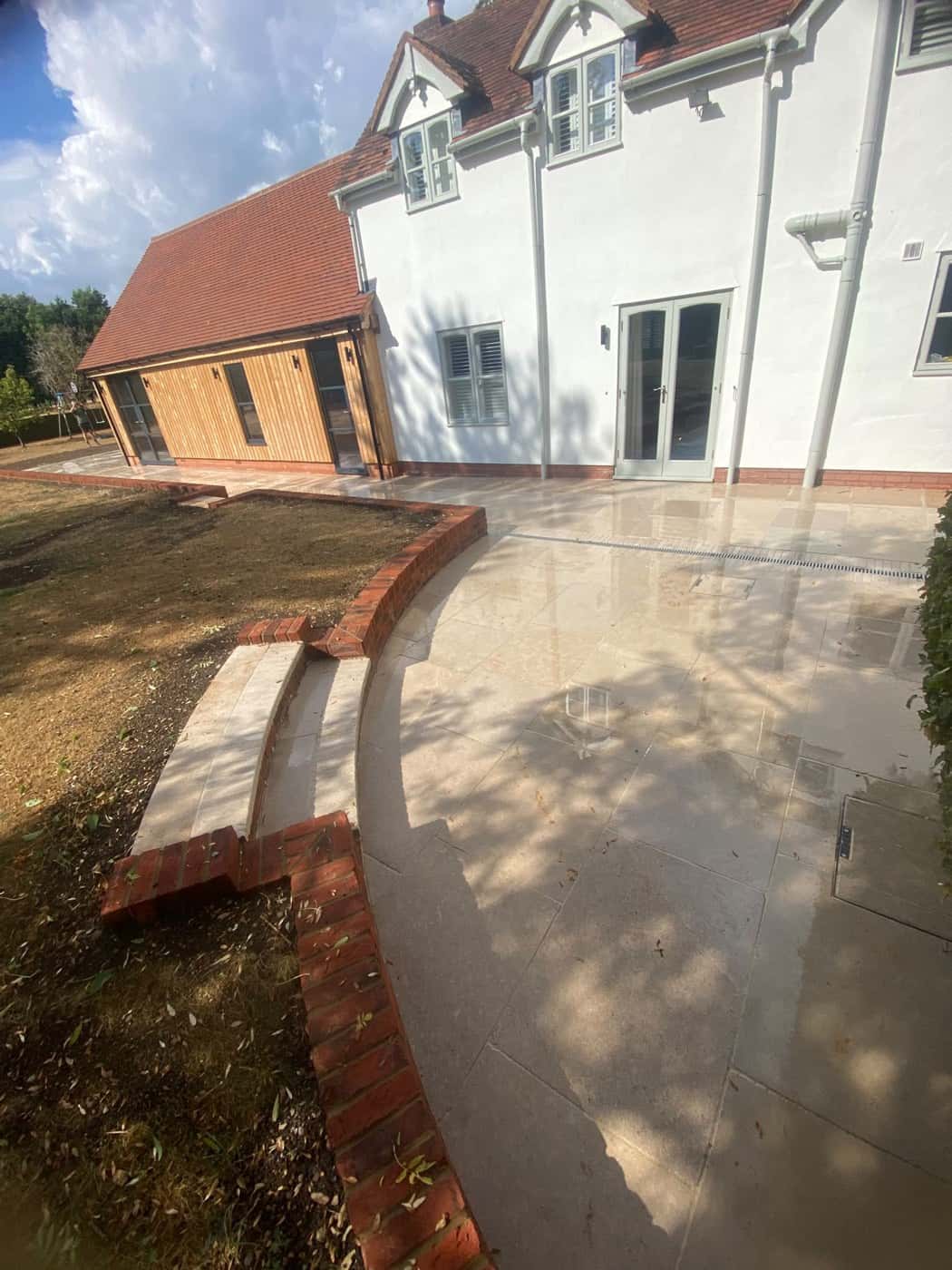 Porcelain patio with curved, brick-edged steps down to the lawn