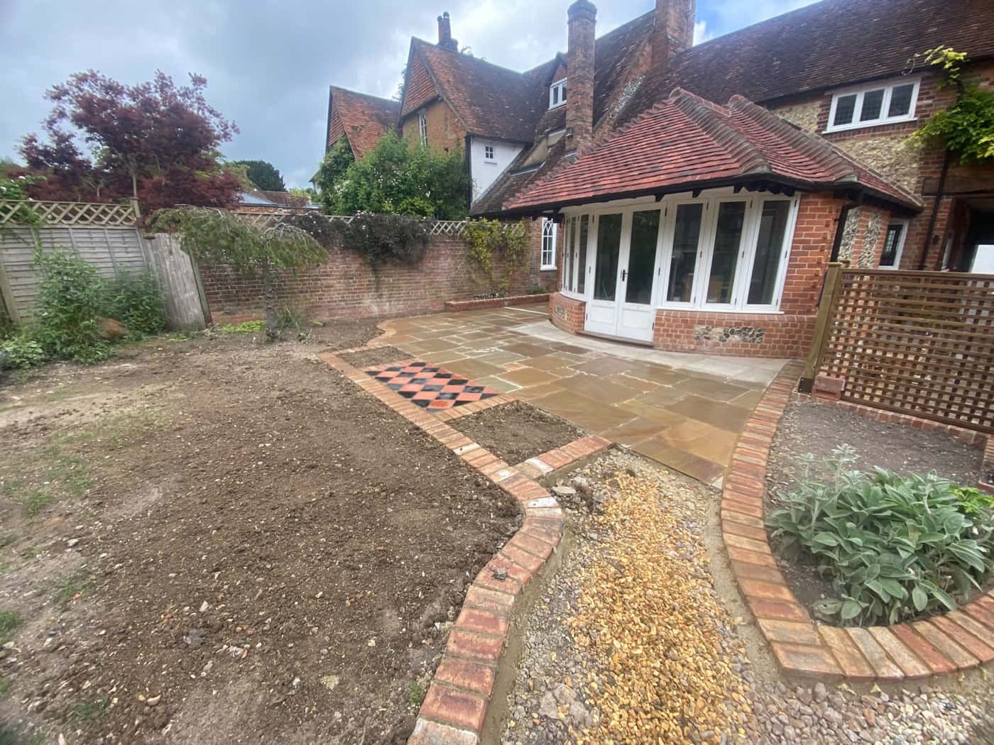 Sandstone patio with a curved, brick-edged gravel path behind a period house