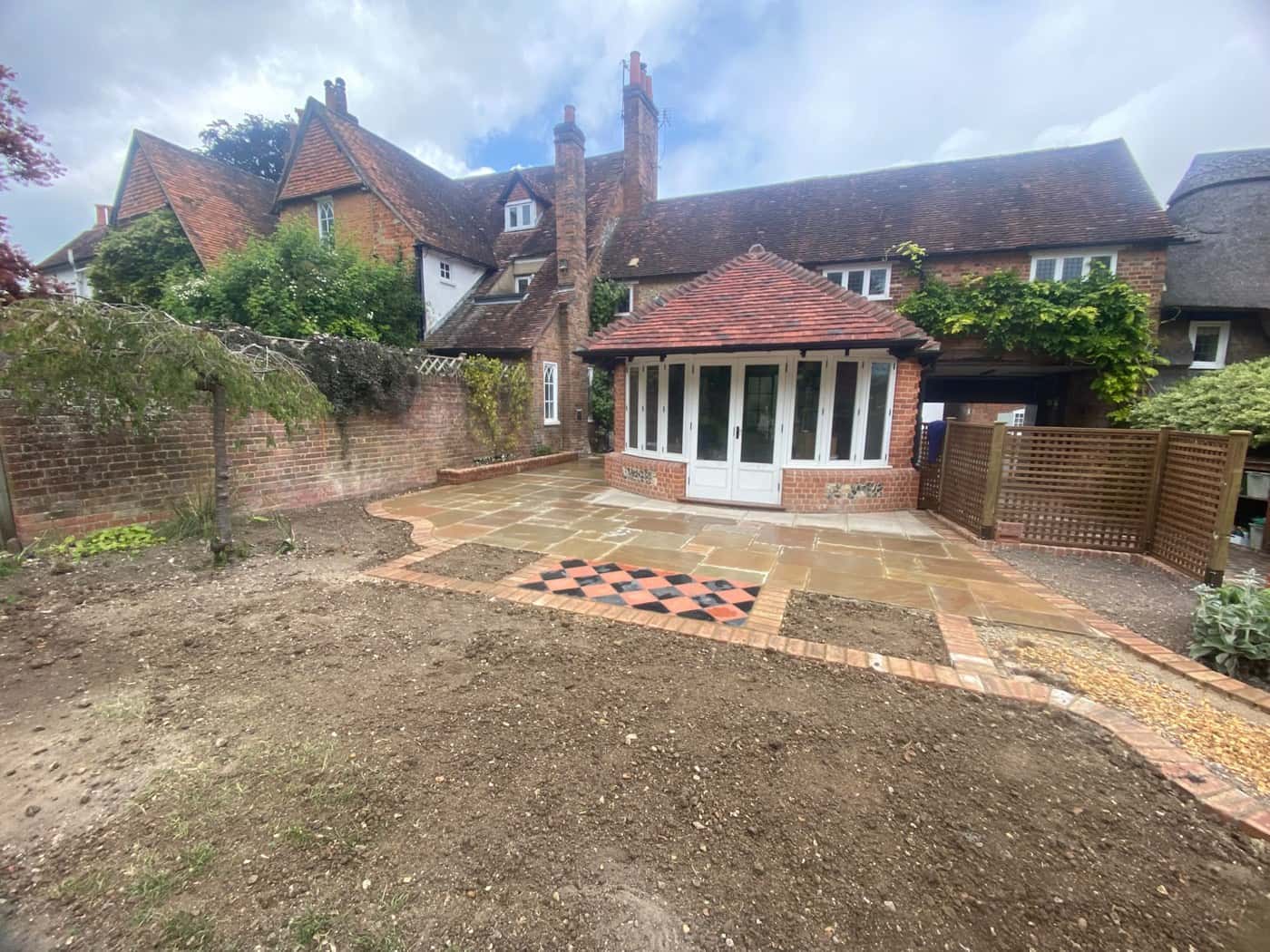 Sandstone patio with brick edging and a chequered tile panel in front of a garden room