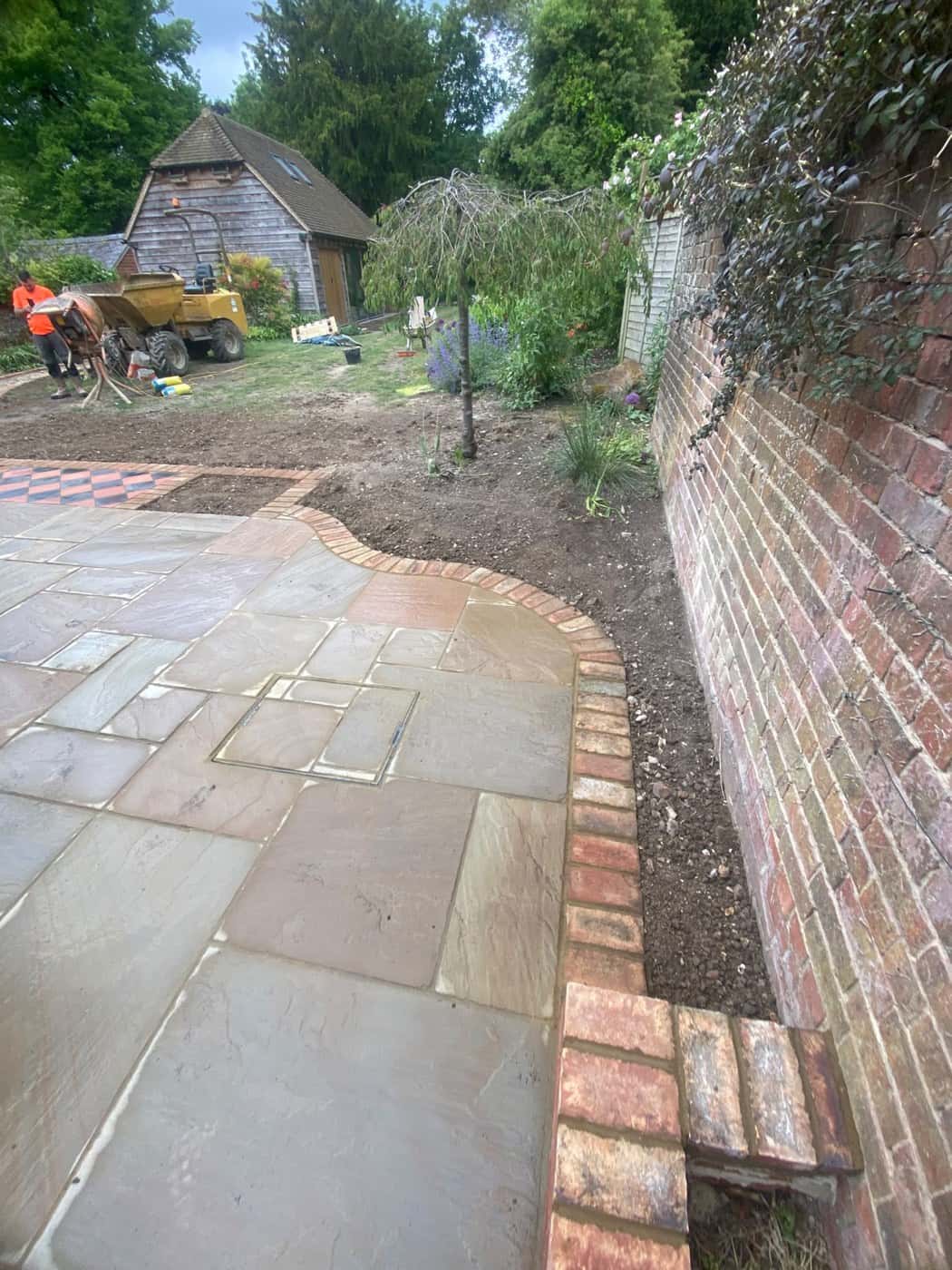Sandstone paving with a curved brick edge beside an old garden wall